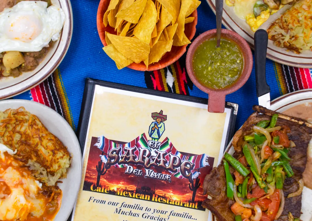 A table of El Sarape Del Valle dishes with chips, salsa and the menu on a sarape